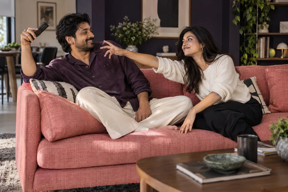 Two fully clothed adults sharing a playful smile as one reaches for the remote.